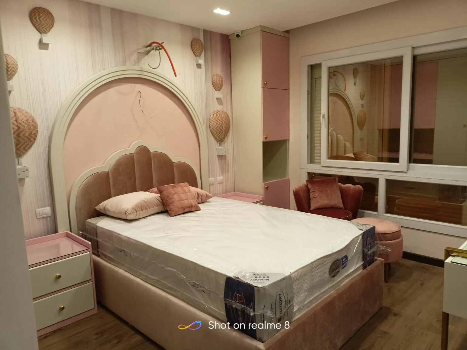 Bright bedroom with pastel pink and white accents, custom cabinetry, and a neat study area.