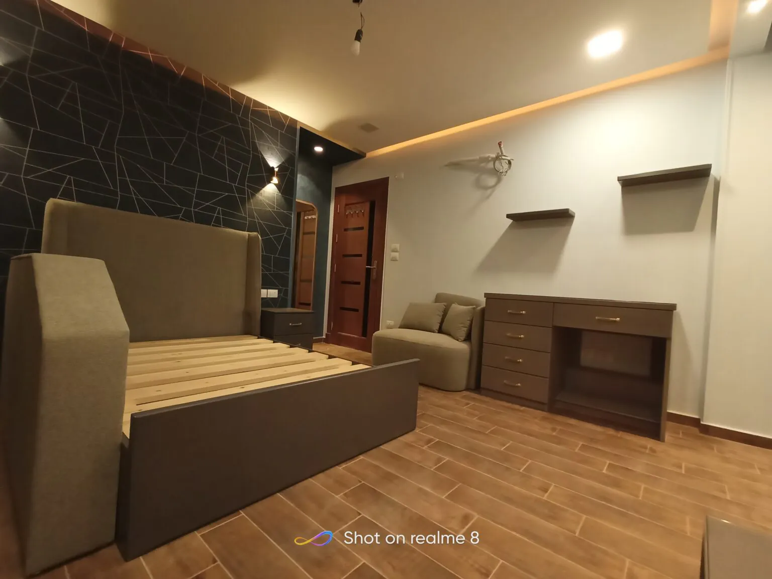 Modern bedroom with a cozy sofa set, a flat-screen TV, and wooden flooring accented with ambient lighting from Consept Art's site work portfolio.