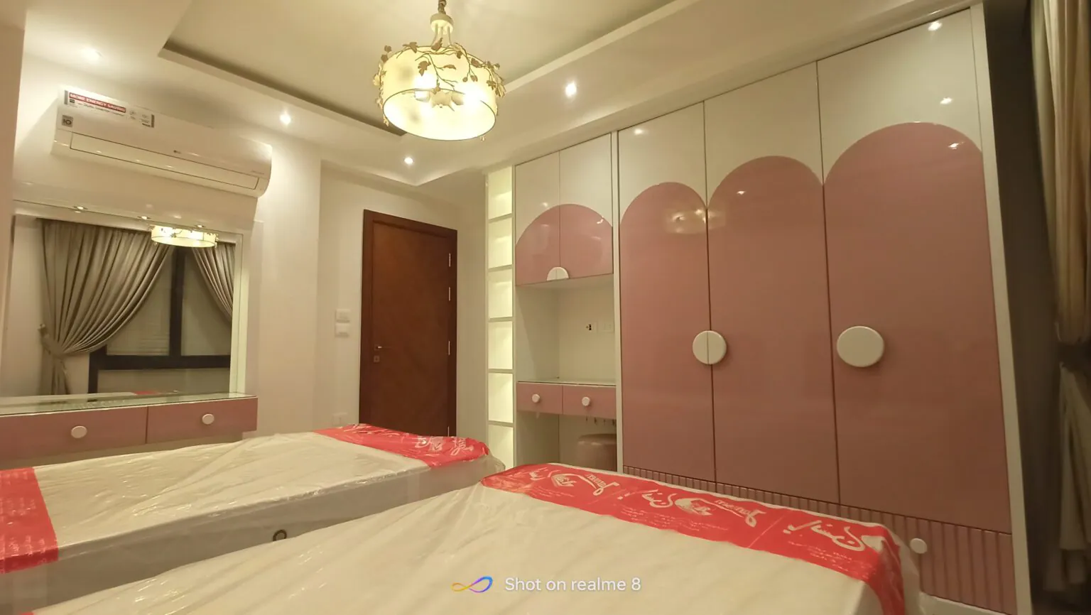 Luxurious master bedroom with pink upholstered furniture, glossy white wardrobes, and an ambient chandelier.