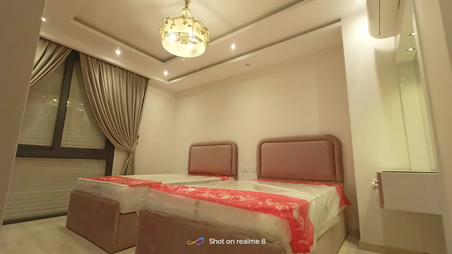 Modern master bedroom featuring a red bedspread, a spacious layout, and beige curtains.