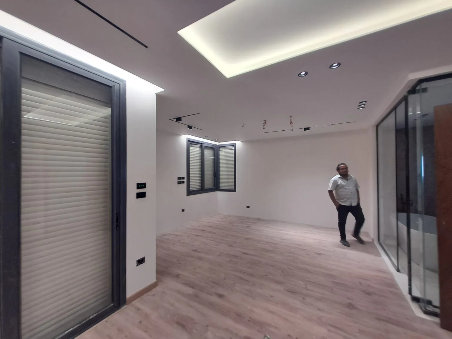 Minimalist room with wooden flooring, a recessed ceiling design, and sliding glass doors.