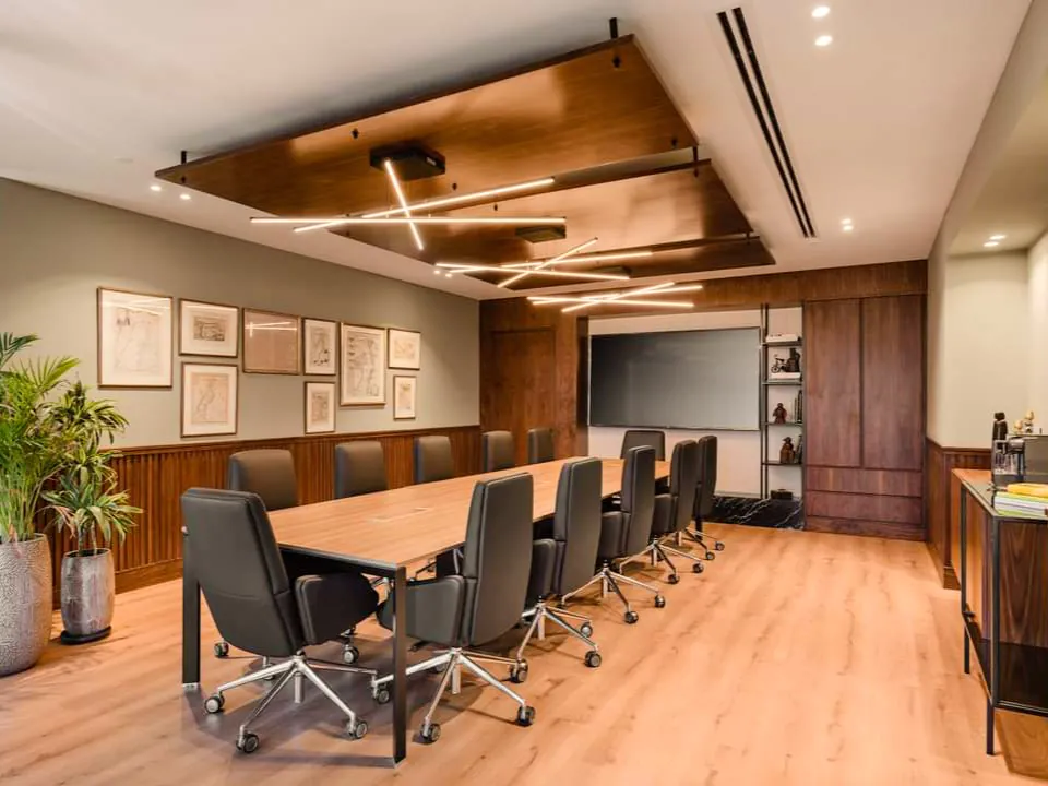 Spacious conference room with a large wooden table, sleek black chairs, and bright recessed lighting. Interior design